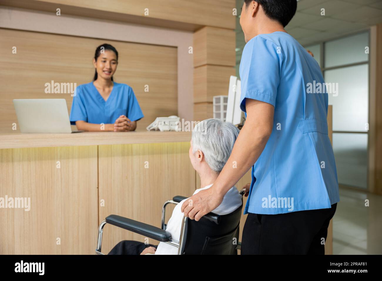 Les patients âgés s'assoient sur un fauteuil roulant et discutent avec une infirmière ou du personnel au comptoir Banque D'Images Les patients âgés s'assoient sur un fauteuil roulant et discutent avec une infirmière ou du personnel au comptoir Banque D'Images
