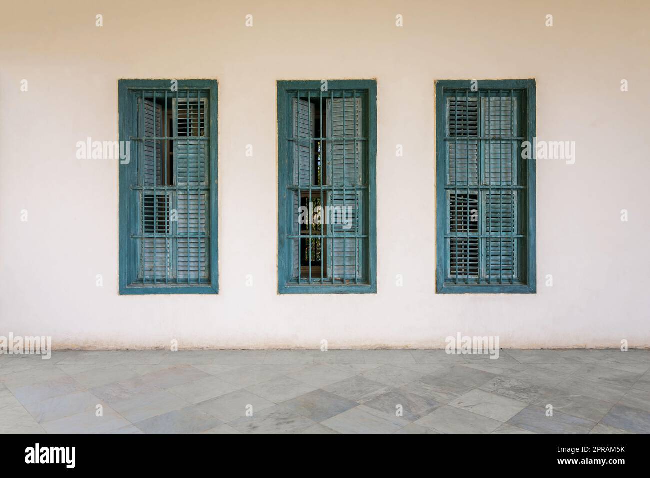 Mur blanc avec trois volets en bois vert grunge, barres en fer forgé et sol en marbre Banque D'Images