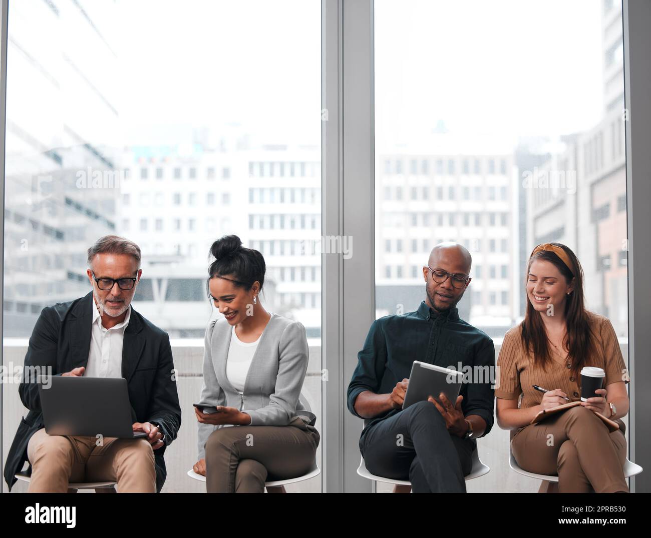 Vous êtes assis en présence de la grandeur. Un groupe de jeunes hommes d'affaires utilisant des appareils numériques tout en attendant dans la file d'attente. Banque D'Images