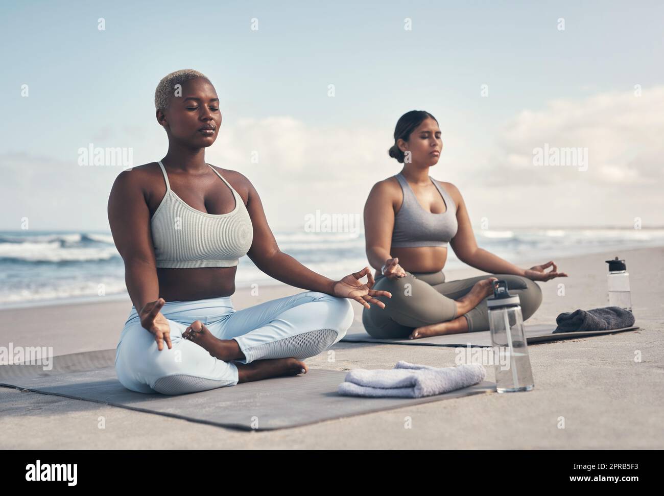 Je me sens en paix quand je suis autour de vous. Deux jeunes femmes méditant pendant leur routine de yoga sur la plage. Banque D'Images
