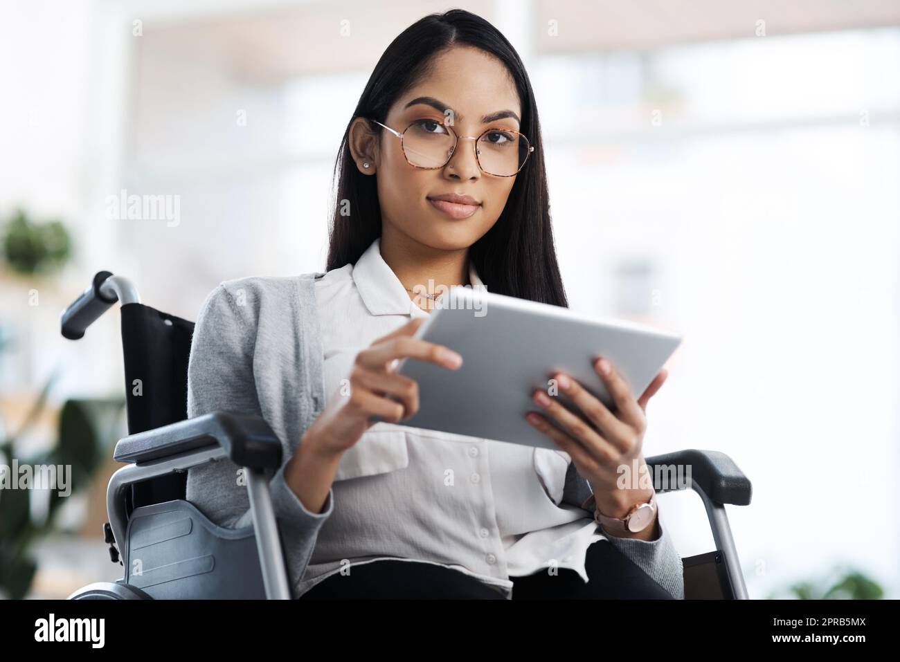 Axé sur la voie à suivre. Portrait court d'une jeune femme d'affaires attirante dans un fauteuil roulant en utilisant sa tablette au bureau. Banque D'Images