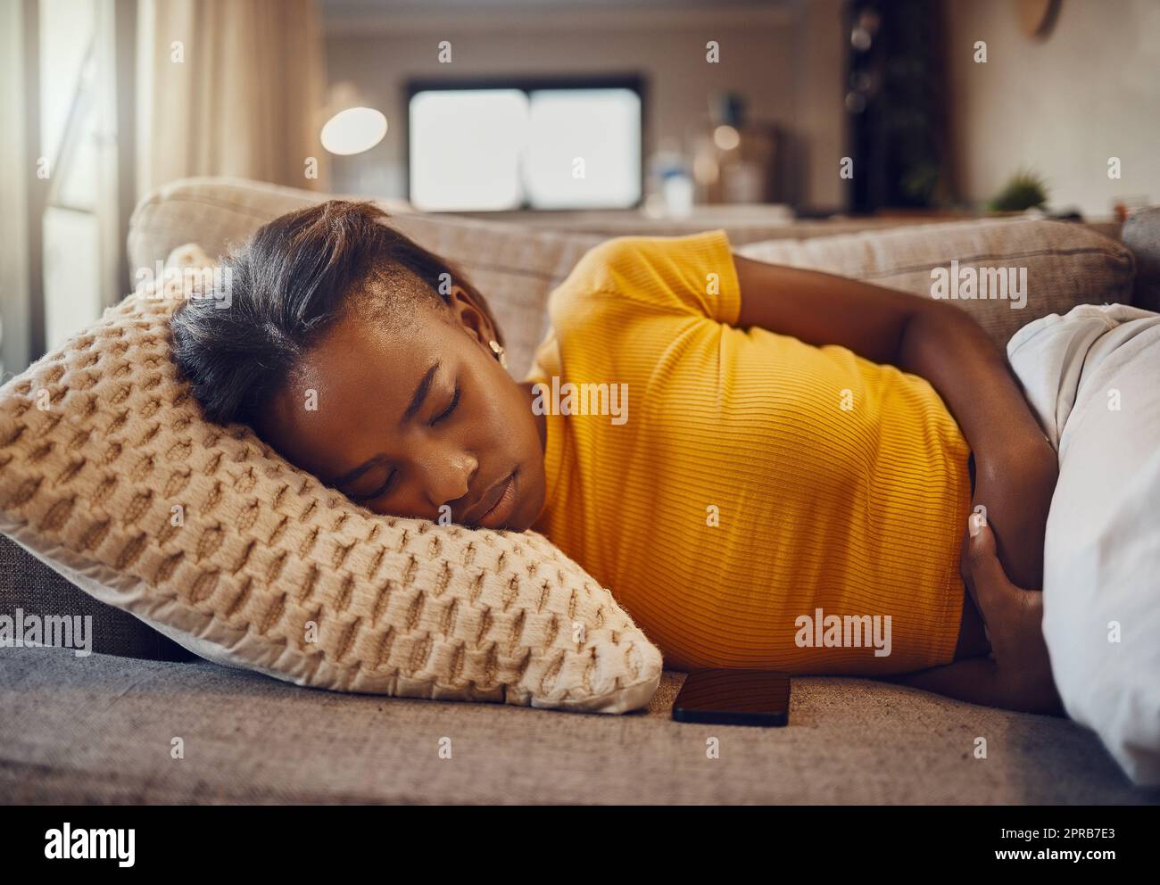 Douleurs à l'estomac, maladie et maladie entraînant le sommeil, la sieste et le repos d'une femme noire, jeune et somnolente sur un canapé à la maison. Femme détendue, malade ou malade souffrant de la fatigue du covid pendant la sieste Banque D'Images