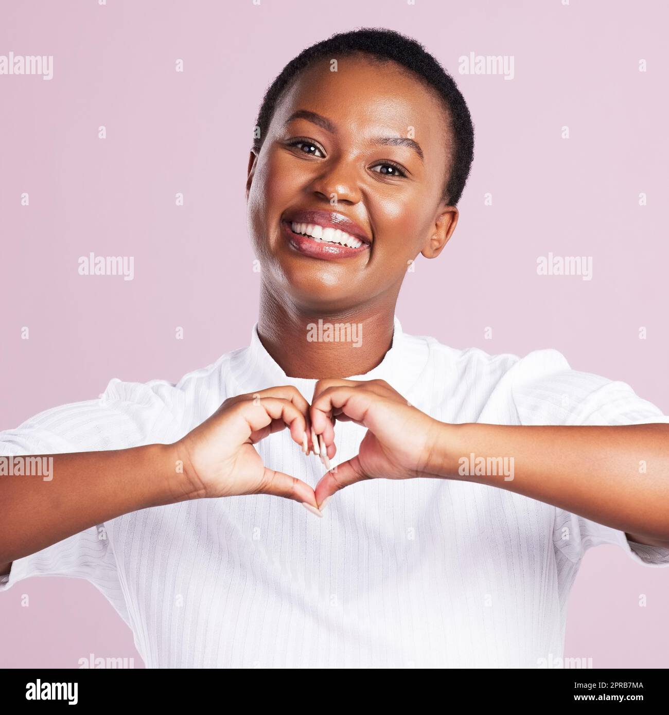 Vous envoyer beaucoup d'amour. Portrait d'une jeune femme faisant un geste de coeur avec ses mains contre un fond rose. Banque D'Images