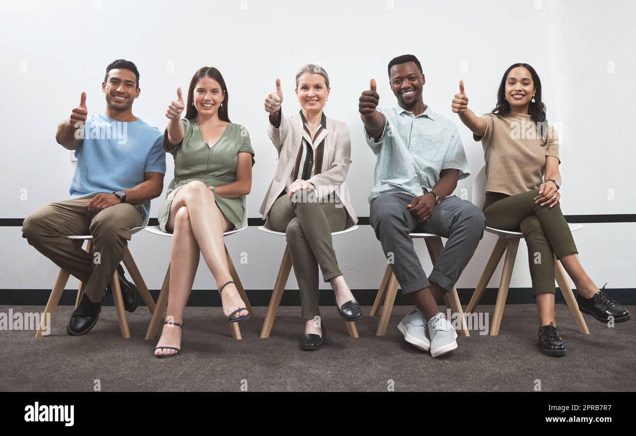 Croyez en vous et vous réussirez. Portrait d'un groupe d'hommes d'affaires montrant les pouces tout en étant assis ensemble contre un mur blanc. Banque D'Images