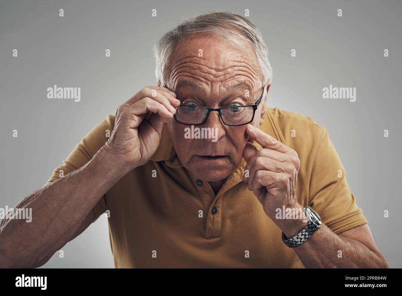 Je suis vraiment vieux. Prise de vue en studio d'un homme âgé qui ajuste ses lunettes sur fond gris. Banque D'Images