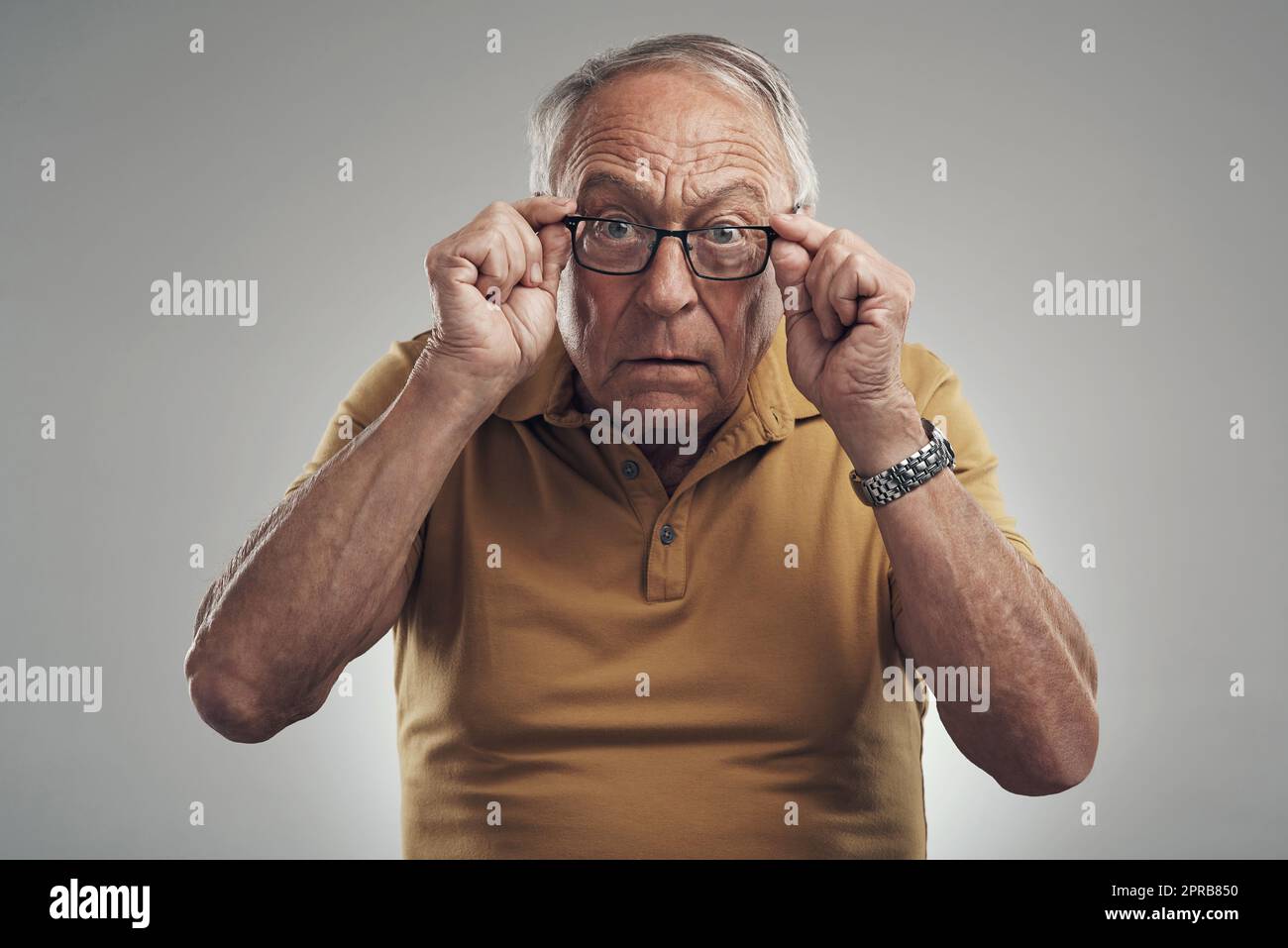 Est-ce un M ou un N. Studio photo d'un homme âgé ajustant ses lunettes sur un fond gris. Banque D'Images