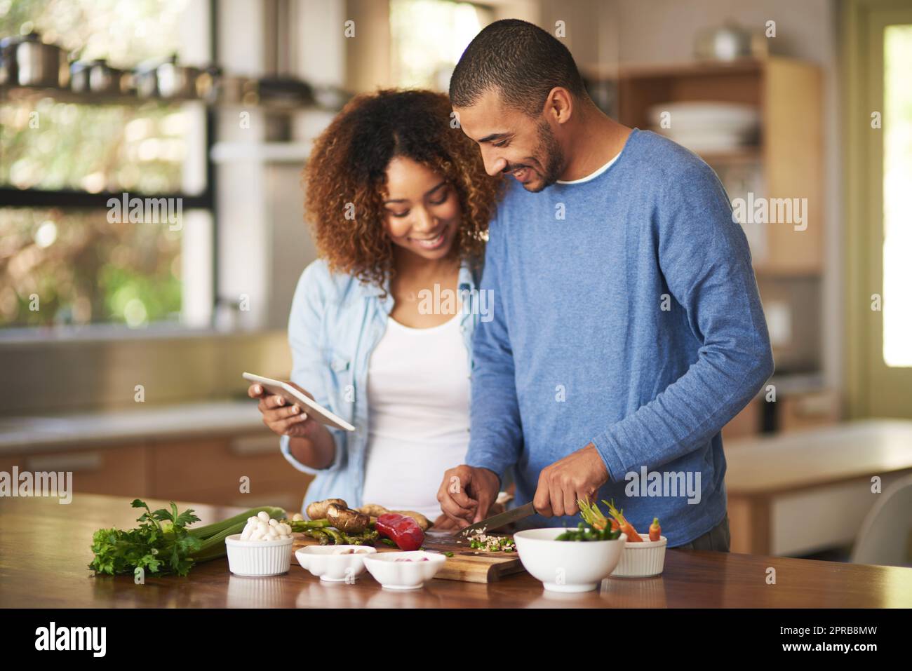 La numérisation de leur régime alimentaire. Prise de vue d'un jeune couple heureux à l'aide d'une tablette numérique tout en préparant un repas sain à la maison. Banque D'Images