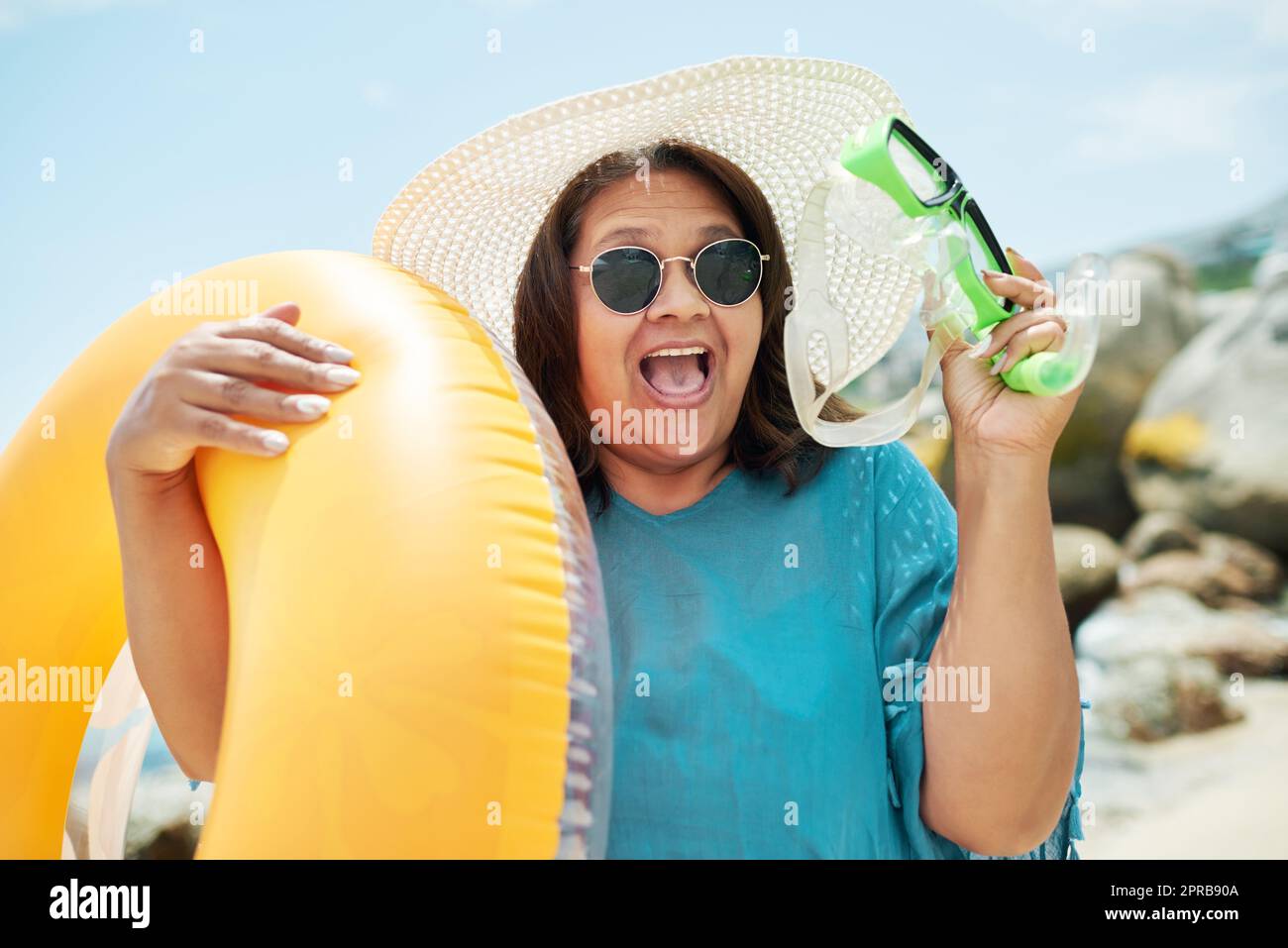 Il est temps de faire du snorkeling. Une femme mature se tenant debout et tenant une piscine gonflable et de la snorkeling pendant une journée sur la plage. Banque D'Images