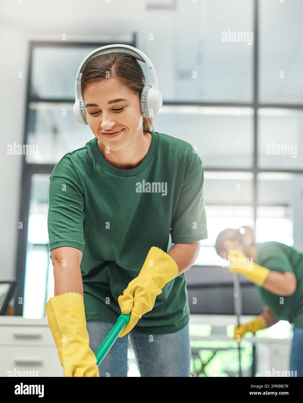 Fournir un environnement de travail propre à chaque client. Une jeune femme nettoyant un bureau avec son collègue en arrière-plan. Banque D'Images