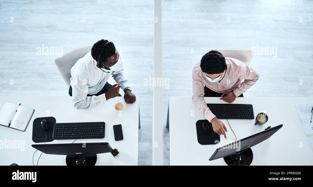 S'aider mutuellement à distance de sécurité. Prise de vue en grand angle de deux agents de centre d'appels travaillant ensemble dans un bureau. Banque D'Images