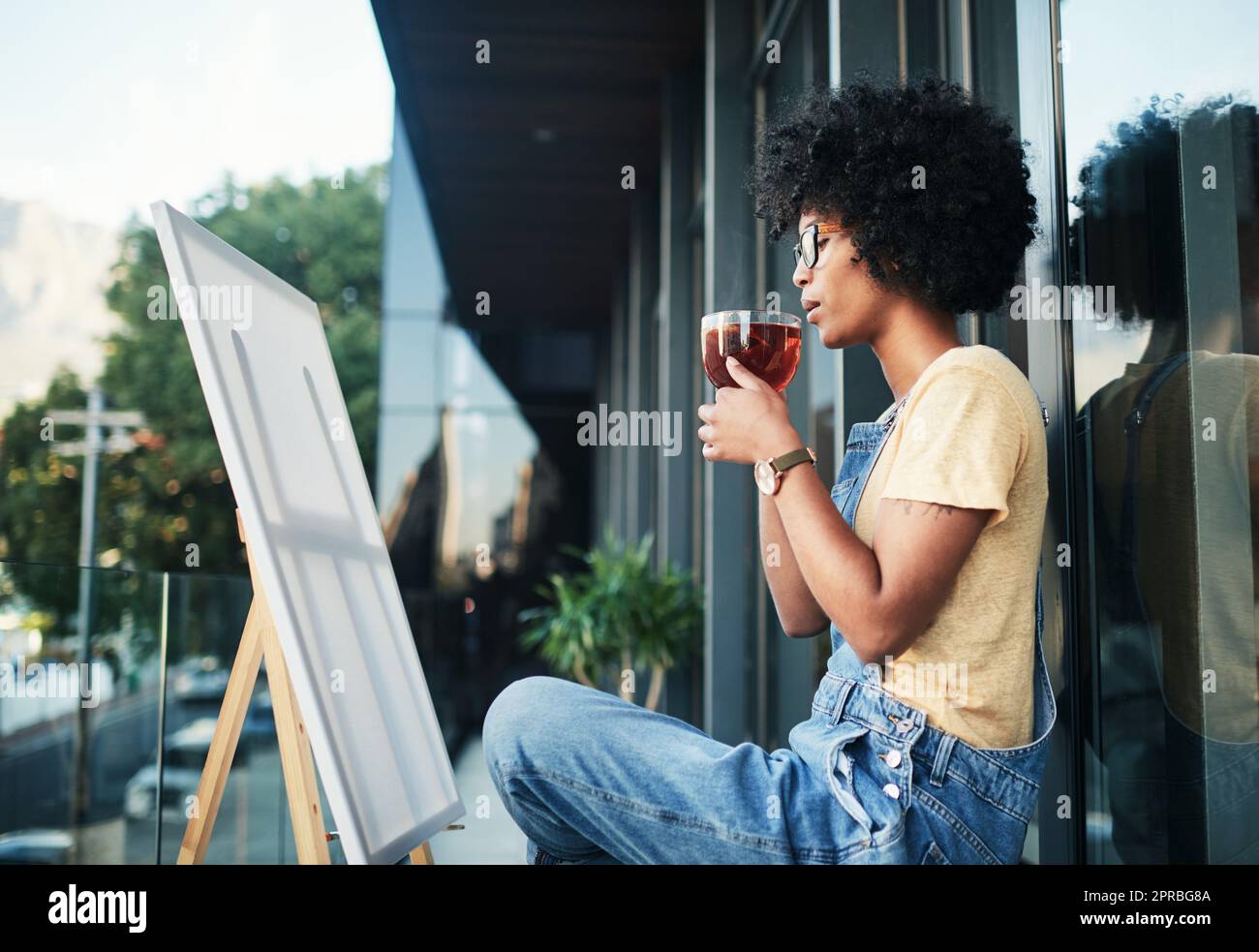 Ces pensées emmêlées attendent d'être démêlées sur la toile. Un jeune artiste ayant le thé tout en étant assis sur le balcon avec une toile. Banque D'Images