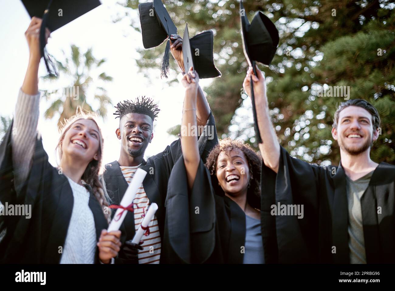 L'éducation est la clé pour déverrouiller la porte d'or de la liberté. Portrait d'un groupe d'étudiants tenant des chapeaux de hausser en célébration le jour de la remise des diplômes. Banque D'Images