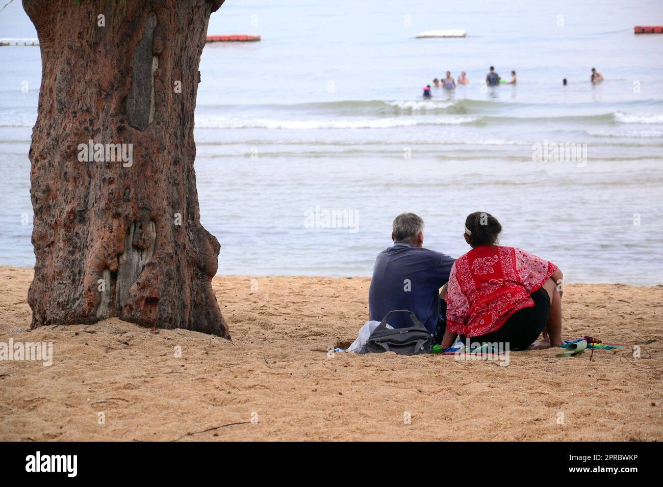 Un homme et une femme plus âgés s'assoient ensemble sur la plage, à côté d'un arbre, en regardant la mer à Jomtien, Pattaya, Thaïlande. Détente, détente, vacances, vacances Banque D'Images