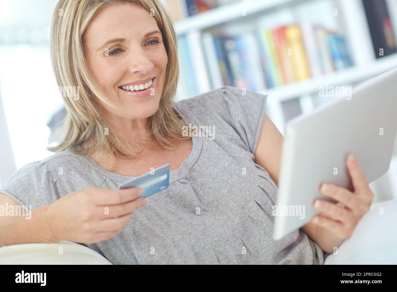 Shopping dans le confort de la maison. une femme mûre attrayante assise avec sa tablette numérique et sa carte de crédit. Banque D'Images