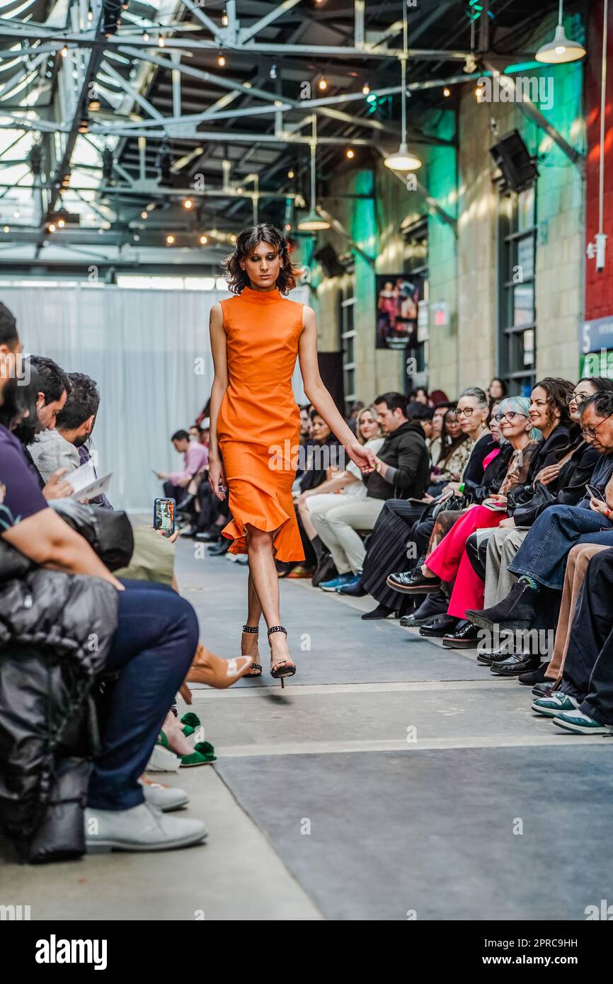 Une robe croisée masculine marchant sur la piste comme modèle dans une robe serrée orange et des talons à bout ouvert Banque D'Images