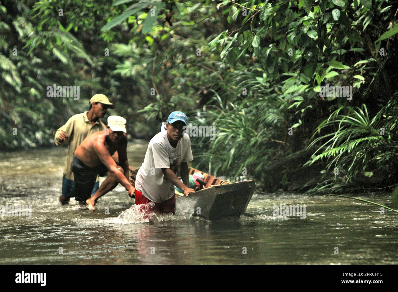 Des hommes qui poussent un bateau pour se déplacer sur les eaux peu profondes de la rivière, à travers la forêt coutumière de la communauté traditionnelle de Dayak IBAN près de Sungai Utik à Kapuas Hulu, Kalimantan occidental, Indonésie. Fondée sur une croyance et des efforts continus pour protéger leur écosystème environnant (forêt, eau, terre) et leurs traditions culturelles, cette communauté a été considérée comme l'une des communautés autochtones les plus réussies du pays dans la gestion d'activités économiques durables, telles que le tourisme éco-culturel. Banque D'Images