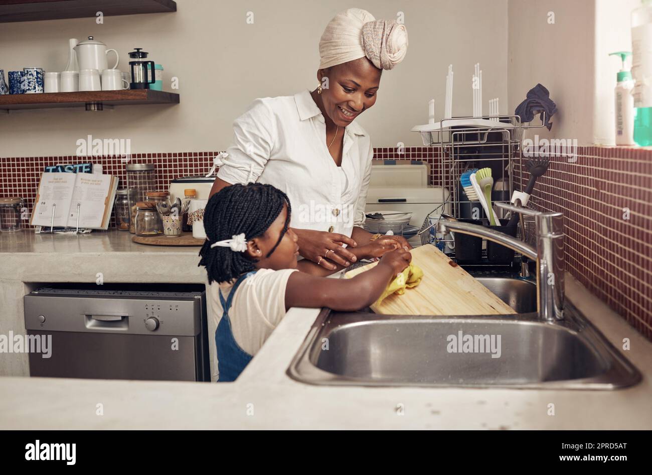 Nous aimons tous les deux une maison propre et hygiénique. Une adorable petite fille aidant sa mère à faire les plats à la maison. Banque D'Images