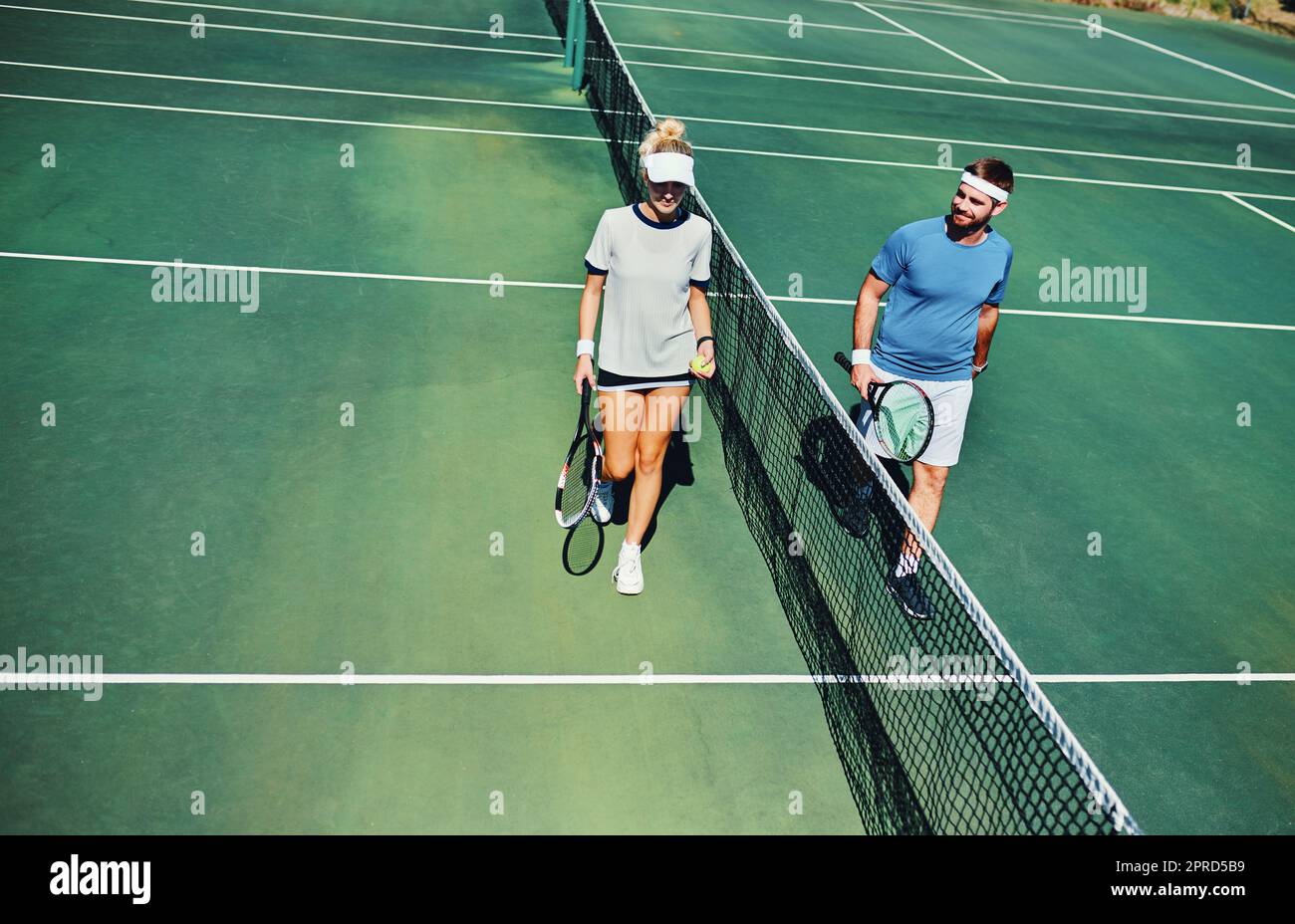 De quel côté êtes-vous ? Prise de vue en longueur de deux jeunes joueurs de tennis parlant tout en marchant ensemble à l'extérieur sur un court de tennis. Banque D'Images