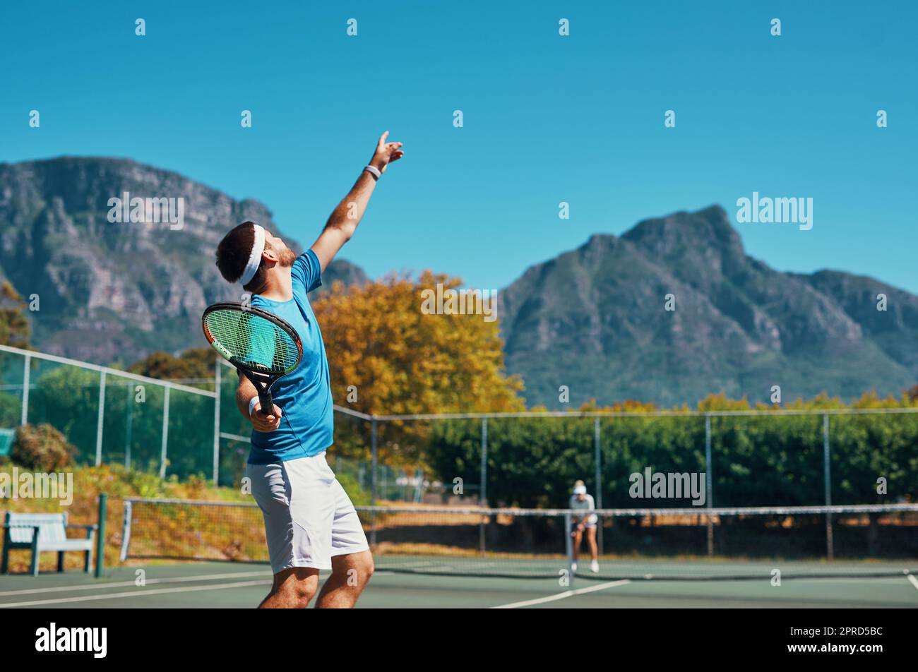 Le timing est tout dans ce sport. Un jeune joueur de tennis masculin se prépare à servir le ballon sur un court de tennis en plein air. Banque D'Images