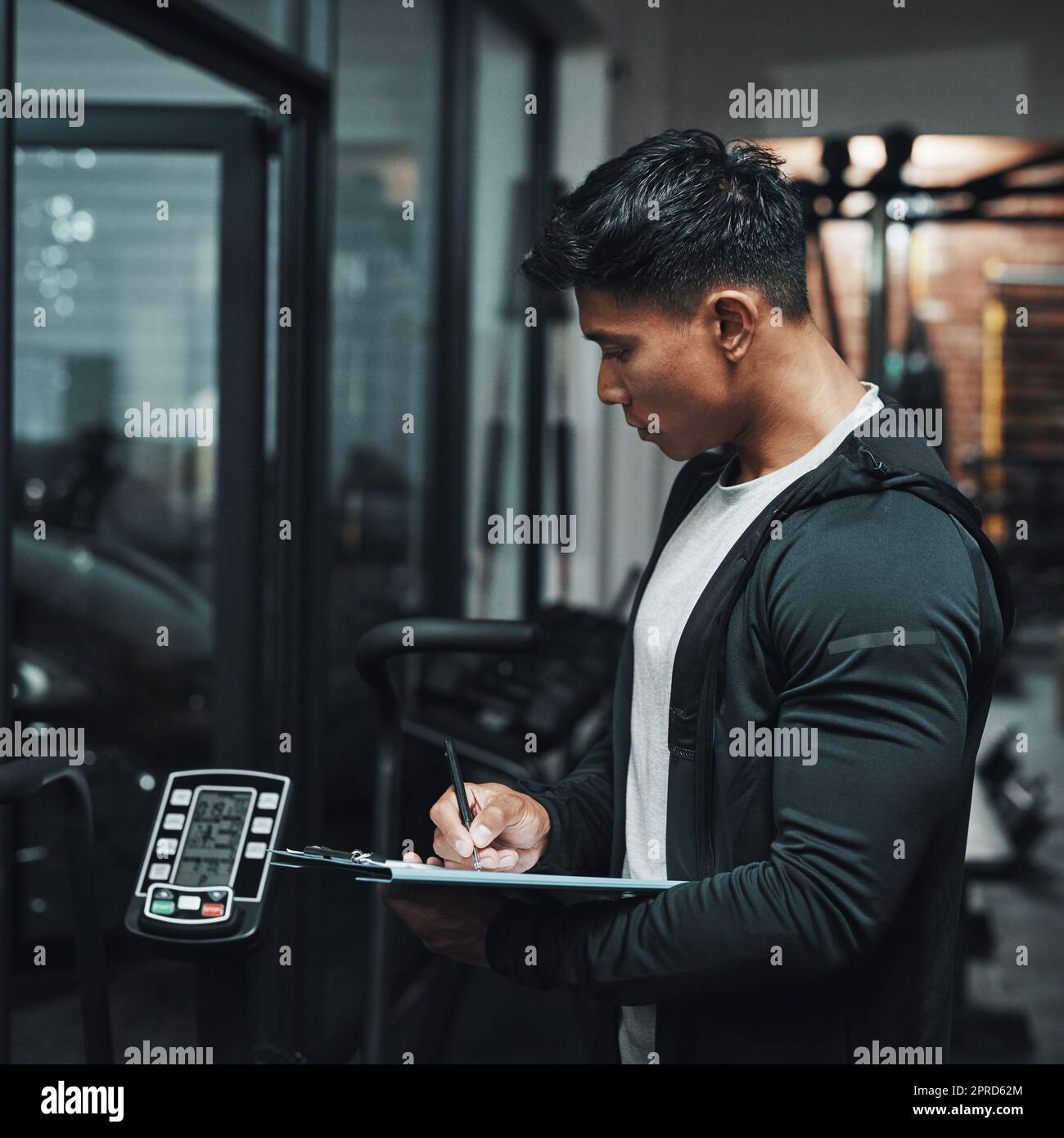 C'est toujours en bon état. Un beau jeune instructeur de fitness masculin inspectant l'équipement d'exercice tout en travaillant dans une salle de gym. Banque D'Images