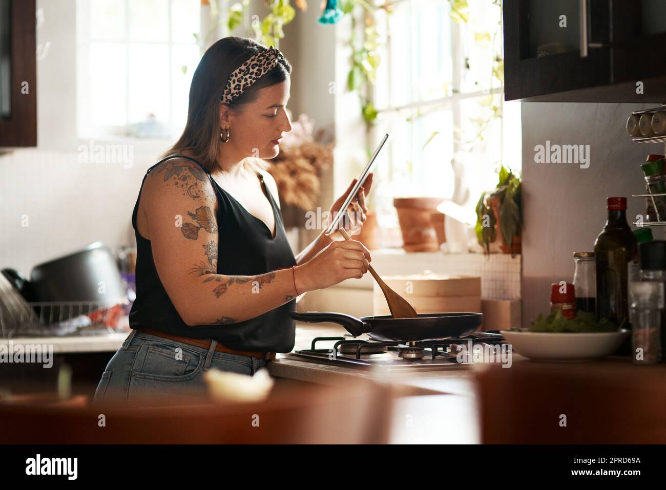 Pas de livre de cuisine, Pas de problème. une jeune femme utilisant une tablette numérique tout en préparant un repas à la maison. Banque D'Images