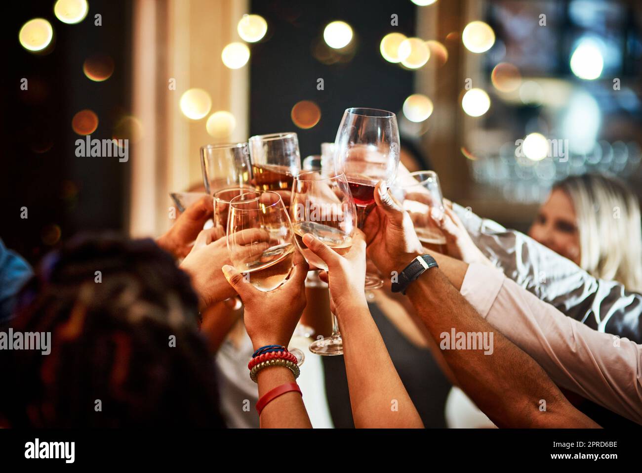 Un groupe d'amis méconnaissables qui ont un toast festif avec leurs boissons dans un bar le soir. Banque D'Images