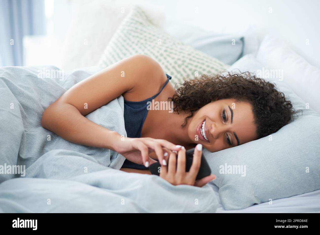 C'est un texte tellement drôle. Une jeune femme attractive qui s'est posée sur le côté au lit et qui utilise son téléphone mobile le matin. Banque D'Images
