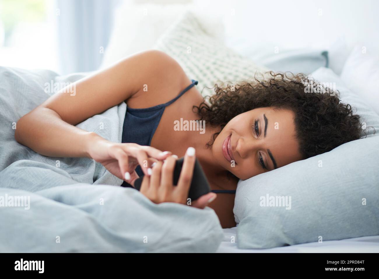 J'ai vérifié mes e-mails du matin. Une jeune femme attirante se couchant sur le côté au lit et utilisant son téléphone mobile le matin. Banque D'Images