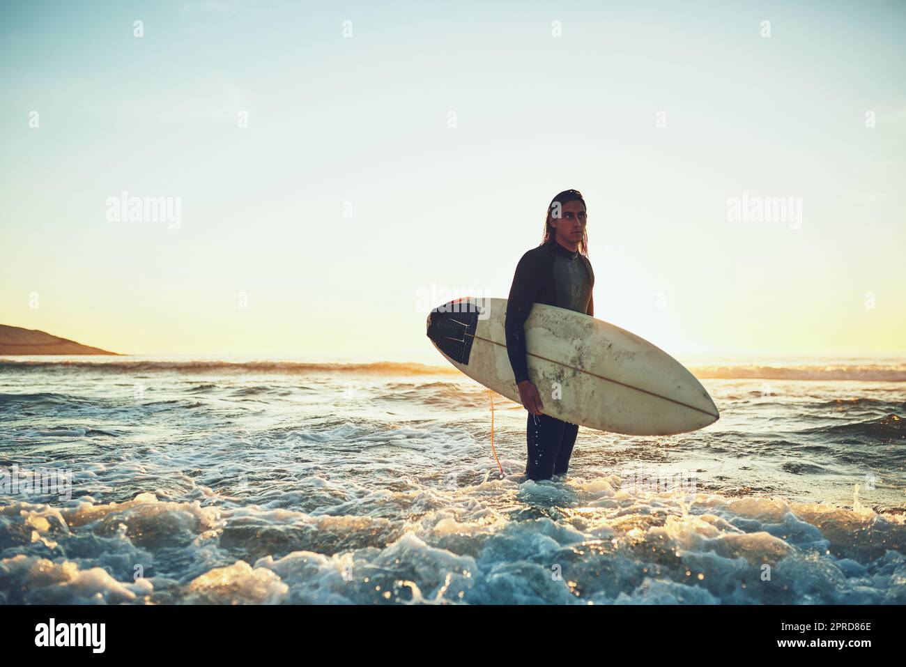 J'aime être dehors dans la grande mer bleue. Un jeune homme portant une planche de surf à la plage. Banque D'Images