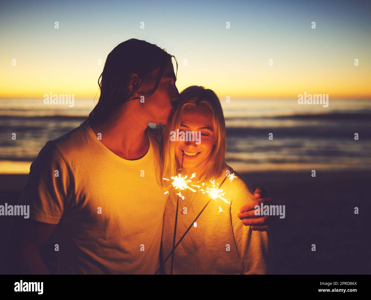 Chaque moment est rendu glorieux par la lumière de l'amour. Un jeune couple jouant avec des spameurs sur la plage la nuit. Banque D'Images