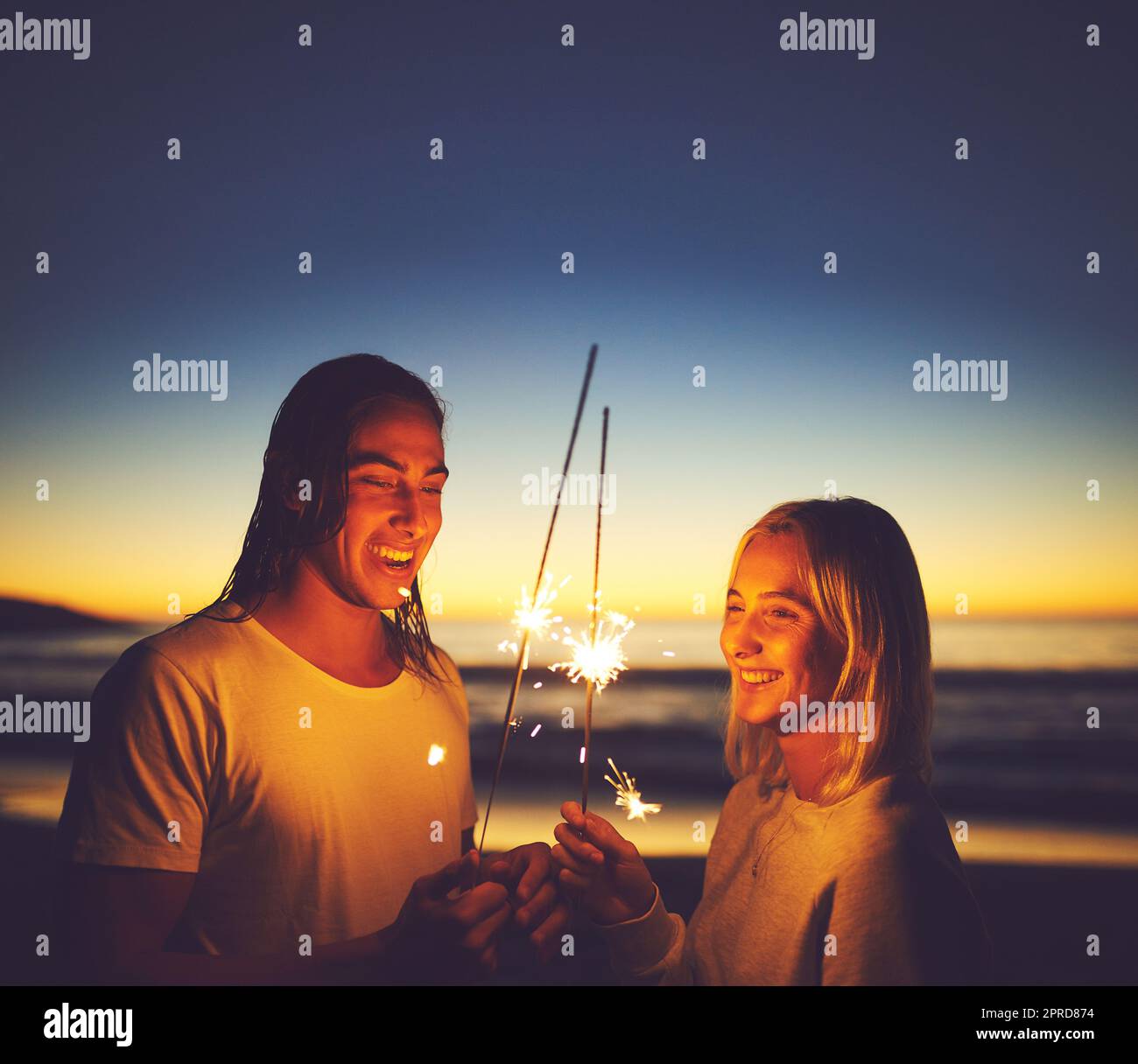Gardez l'étincelle vivante. Un jeune couple jouant avec des spameurs sur la plage la nuit. Banque D'Images