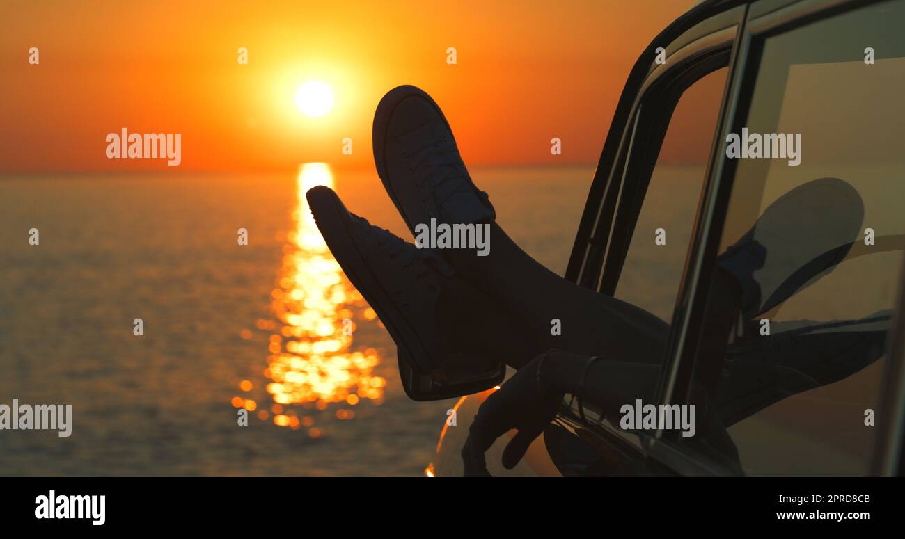 C'est juste vous, le soleil et l'océan. Des jambes de womans méconnaissables danchant par la fenêtre d'une voiture à la plage. Banque D'Images