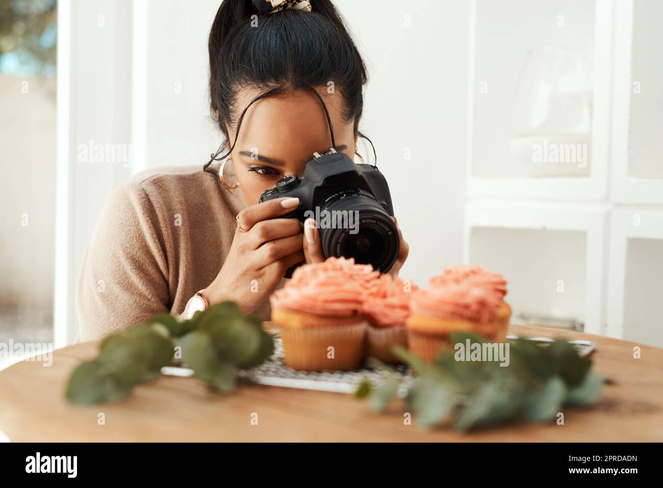 Cela va paraître si bon sur mon blog. Une jeune femme d'affaires attrayante utilisant son appareil photo pour photographier des cupcakes pour son blog. Banque D'Images