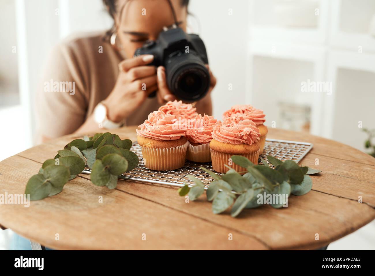Je m'assure d'obtenir le bon angle. Une jeune femme d'affaires attrayante utilisant son appareil photo pour photographier des cupcakes pour son blog. Banque D'Images