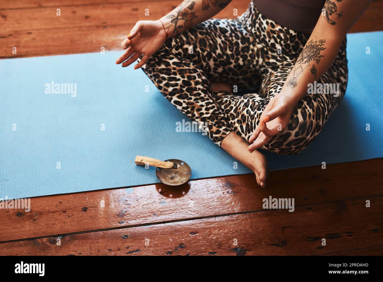 Nettoyage de l'espace autour d'elle pour favoriser la relaxation profonde. Gros plan d'une femme brûlant un bâton de palo santo tout en méditant sur un tapis de yoga à la maison. Banque D'Images