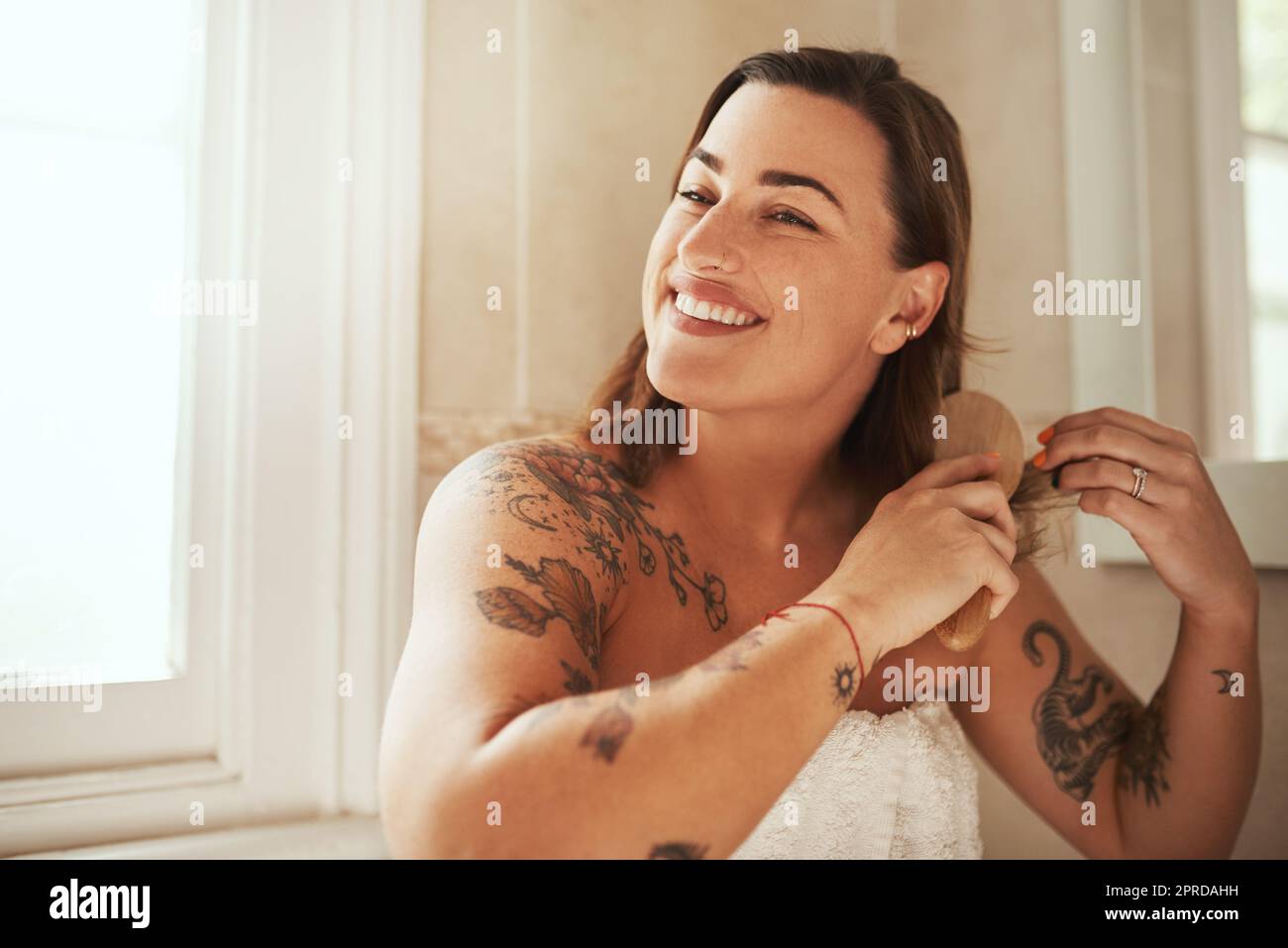 Les effets d'un après-shampooing. Une jeune femme attrayante se brossant les cheveux pendant sa routine de beauté matinale à la maison. Banque D'Images