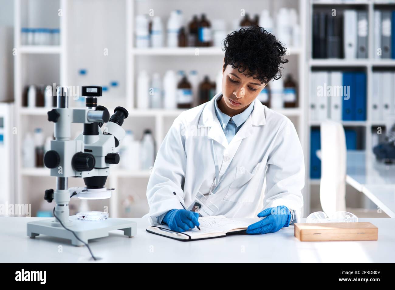 Enregistrer un nouvel ensemble de résultats. Un jeune scientifique écrit des notes tout en travaillant dans un laboratoire. Banque D'Images