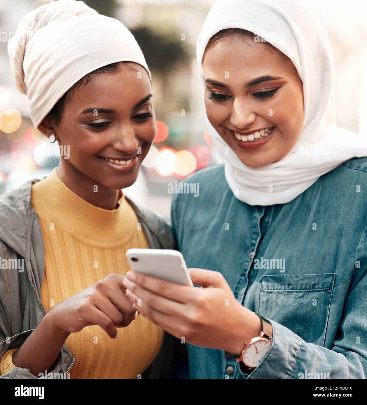 Allons voir cet endroit. Deux jeunes femmes attrayantes portant un foulard et debout ensemble tout en utilisant un téléphone cellulaire dans la ville. Banque D'Images