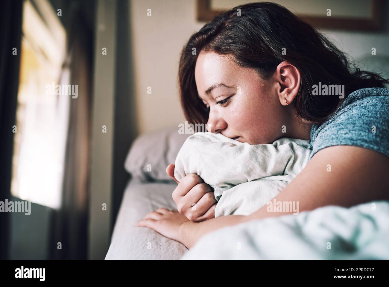 Elle s'est réveillée avec un cœur brisé. Une jeune femme attrayante regardant déprimé tout en étant allongé sur son lit à la maison. Banque D'Images
