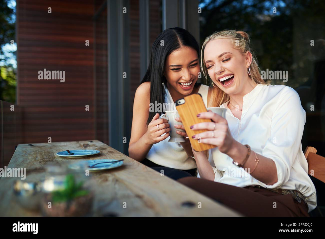 Tout semble plus drôle quand vous êtes haut sur le café. Deux jeunes femmes regardant quelque chose sur un téléphone portable tout en étant assis dans un café. Banque D'Images