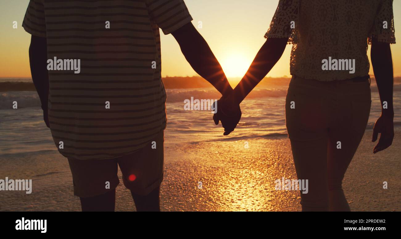 Notre amour est plus profond que l'océan. Vue arrière d'un jeune couple méconnu tenant les mains sur la plage au coucher du soleil. Banque D'Images