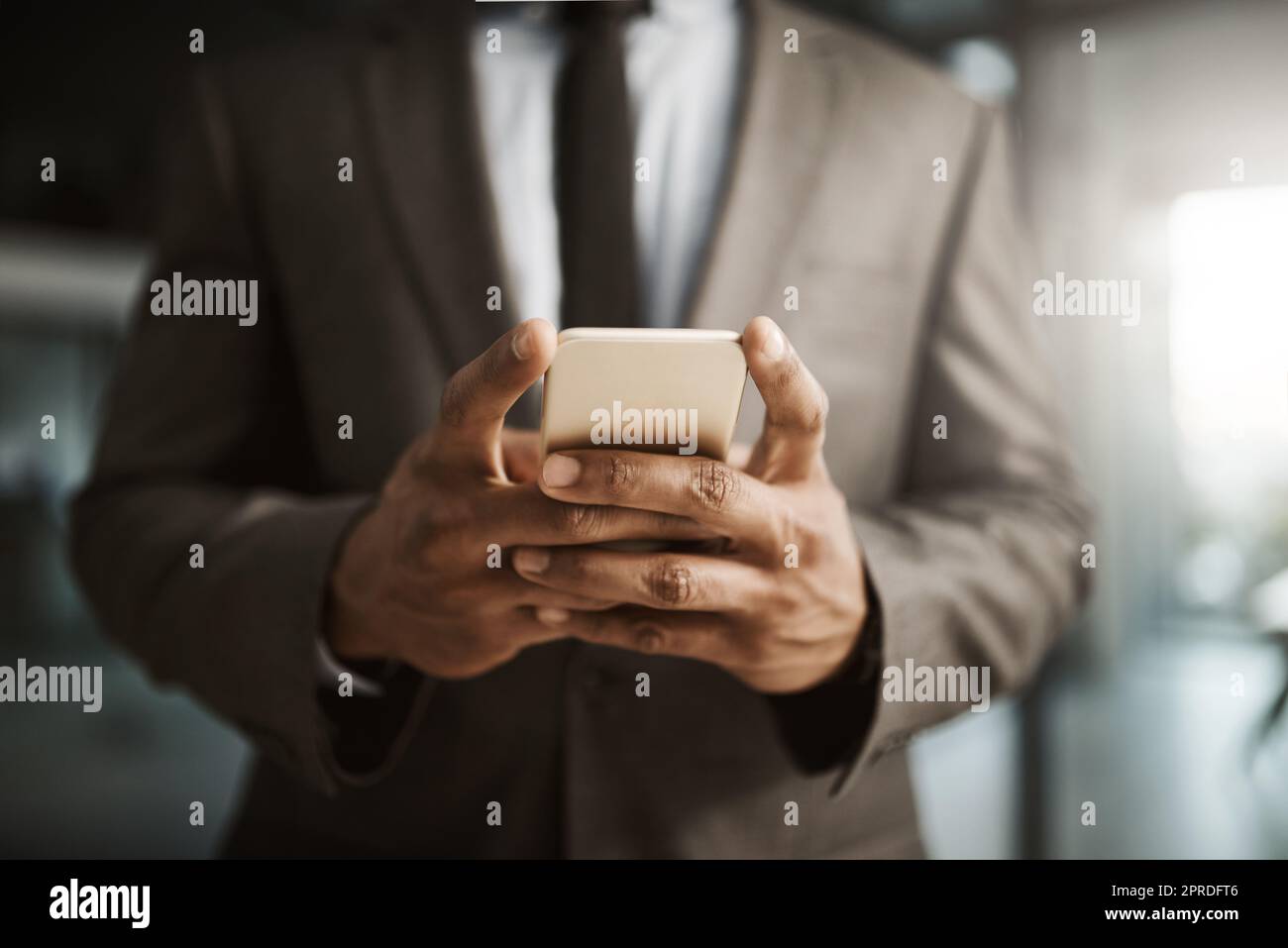 Un homme d'affaires envoie un SMS sur un téléphone pour envoyer un SMS professionnel formel à l'intérieur d'un bureau au travail. Un homme de direction d'entreprise africain portant un costume tapant un e-mail à son client en ligne gros plan Banque D'Images