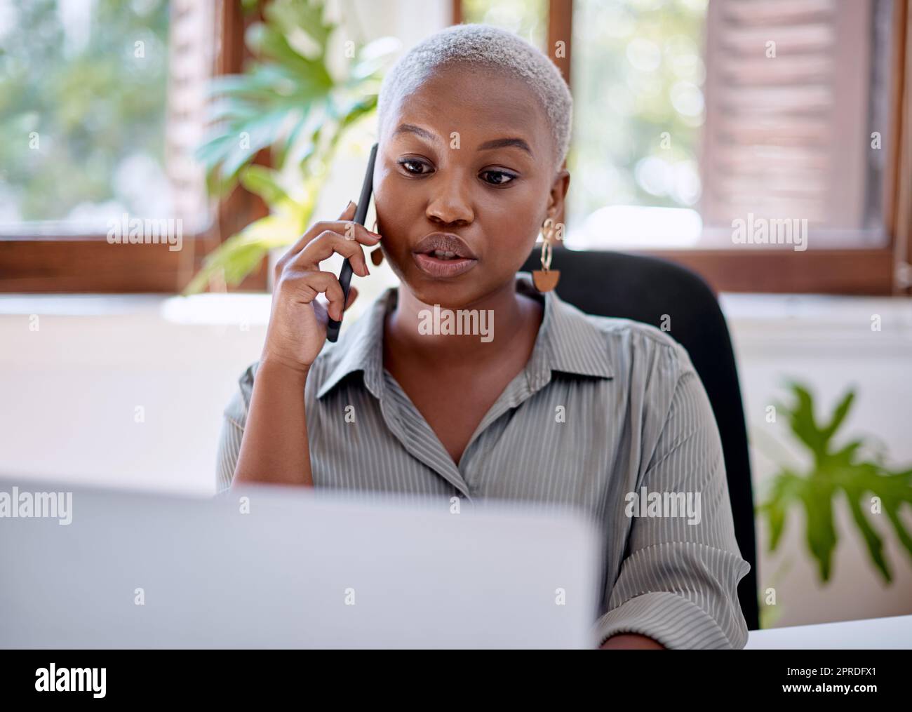 Sa passion s'est accompagnée d'un dévouement sans faille : une jeune femme d'affaires qui parle sur un téléphone portable tout en travaillant sur un ordinateur portable dans un bureau. Banque D'Images