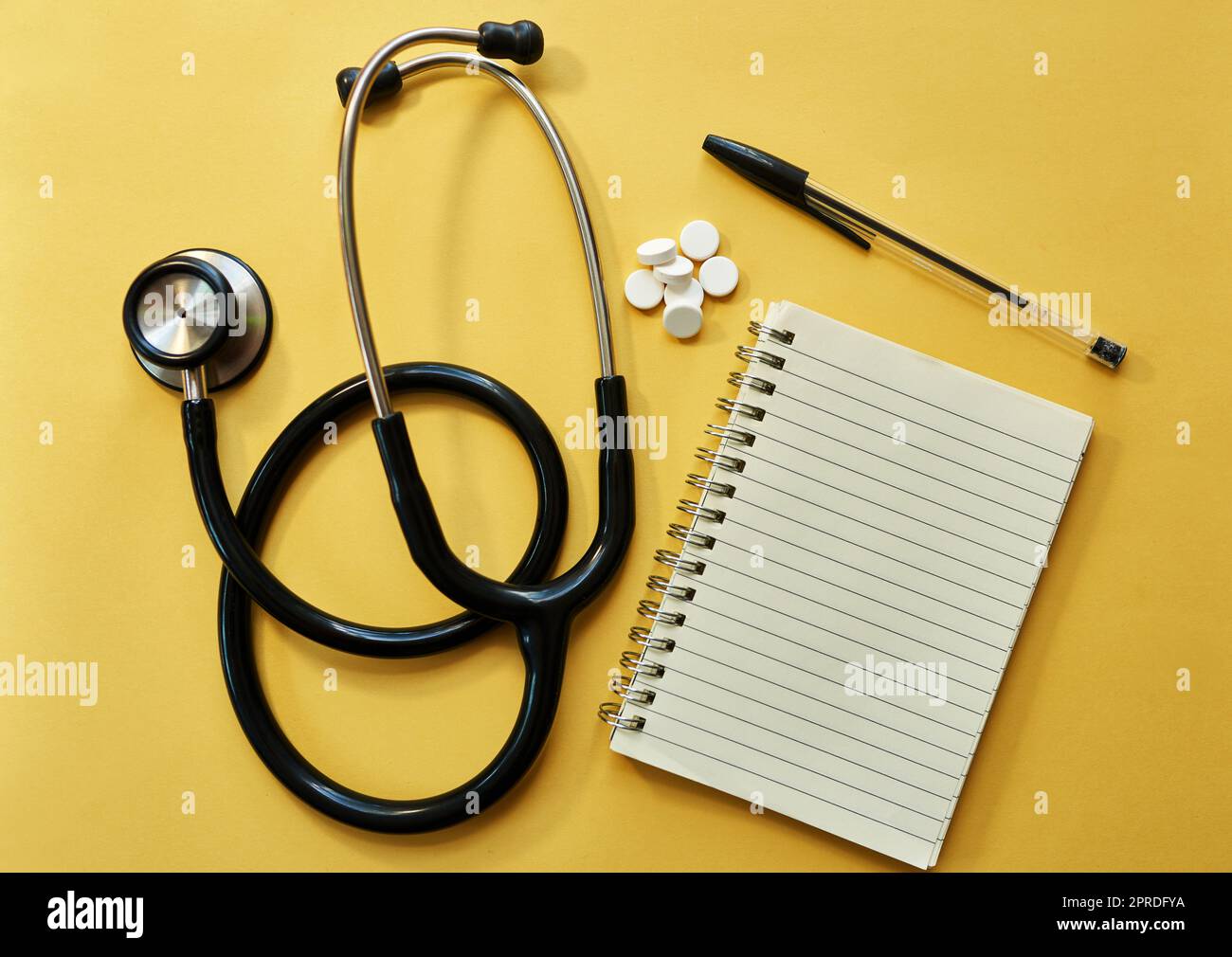 Juste ce que le médecin a prescrit. Studio photo d'un stéthoscope, bloc-notes, stylo et pilules sur fond jaune. Banque D'Images