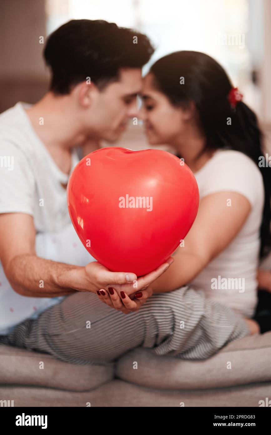 Le jour de la Saint-Valentin a été bien fait. Un jeune couple méconnaissable s'embrasse tout en tenant une montgolfière en forme de cœur le jour de la Saint-Valentin. Banque D'Images