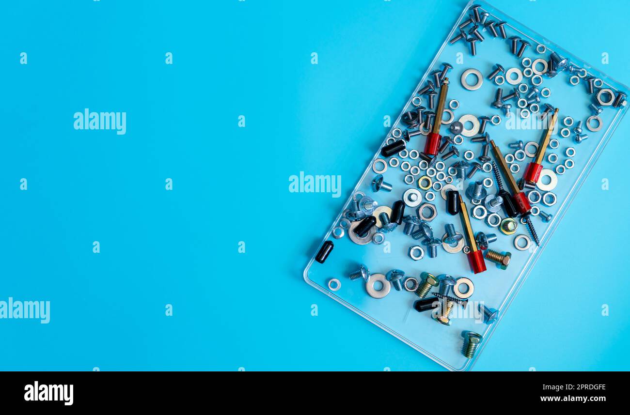 Vue de dessus boulons métalliques, écrous, rondelle et vis dans un plateau en plastique sur fond bleu. Matériel de fixation. Outils matériels des techniciens en mécanique. Accessoires de fixation filetés. Vis et écrous de fixation Banque D'Images