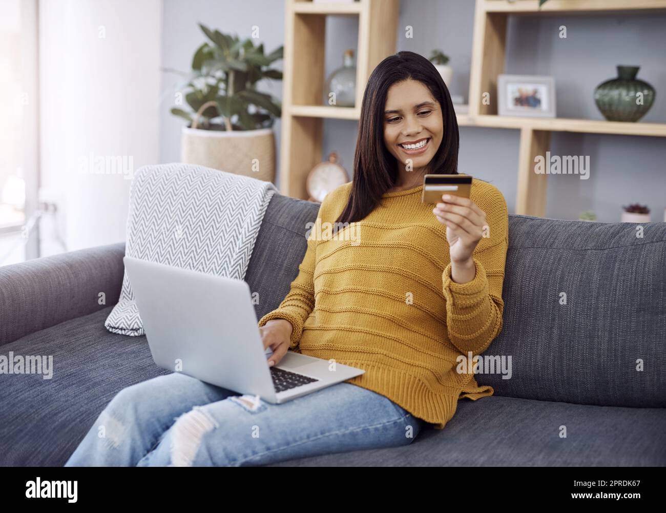 Faire du shopping dans le confort de votre maison. Une jeune femme attrayante fait du shopping en ligne sur son ordinateur portable tout en se relaxant sur un canapé à la maison. Banque D'Images