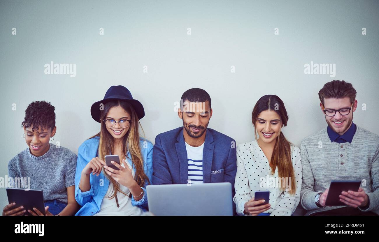 Étaient les meilleurs amis avec les réseaux en ligne. Photo en studio d'un groupe de jeunes hommes d'affaires utilisant la technologie sans fil tout en étant assis dans la ligne sur un fond gris. Banque D'Images