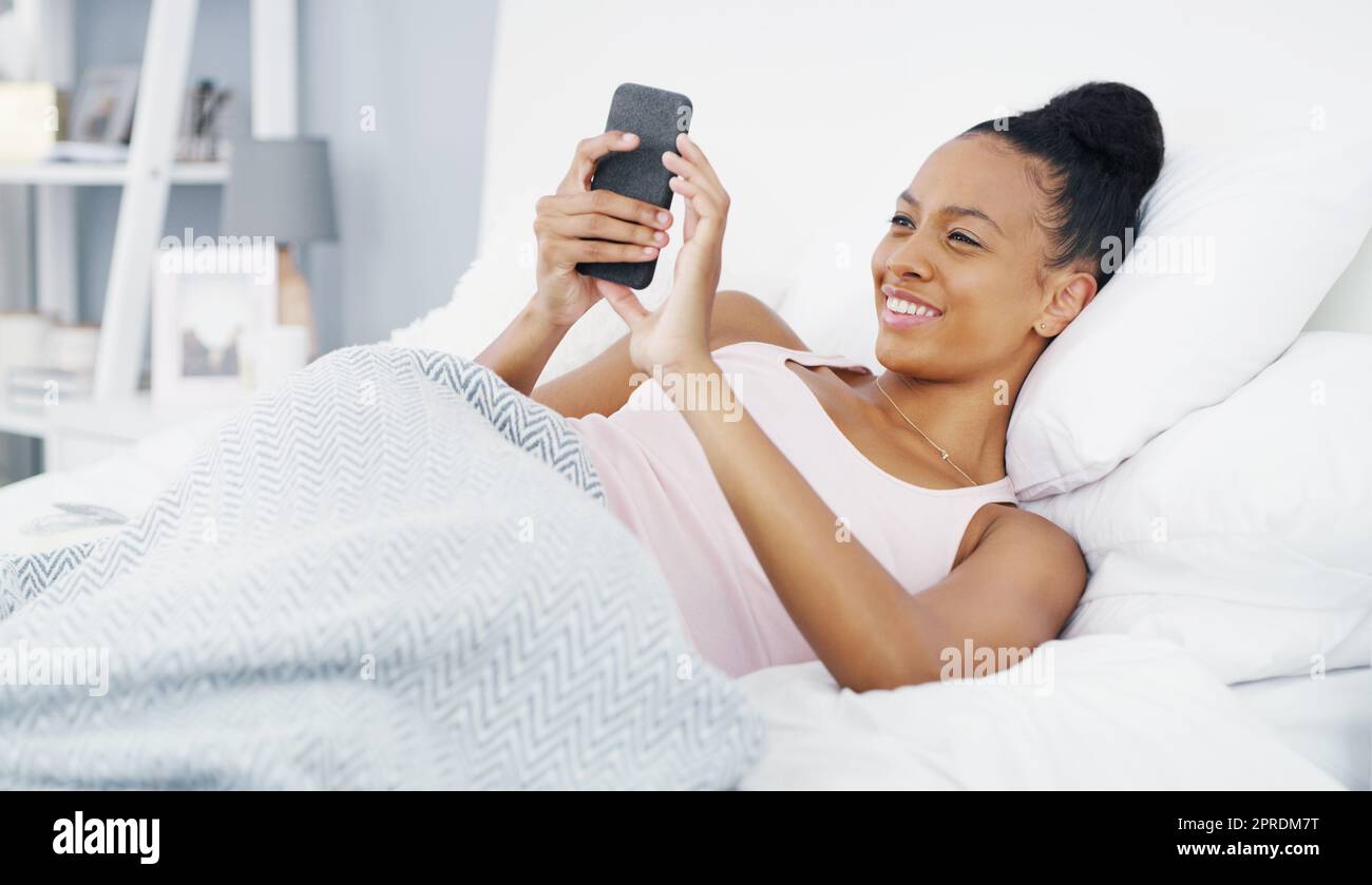 Bonjour à Vous aussi. une jeune femme attirante utilisant son téléphone portable tout en étant couché dans le lit à la maison. Banque D'Images