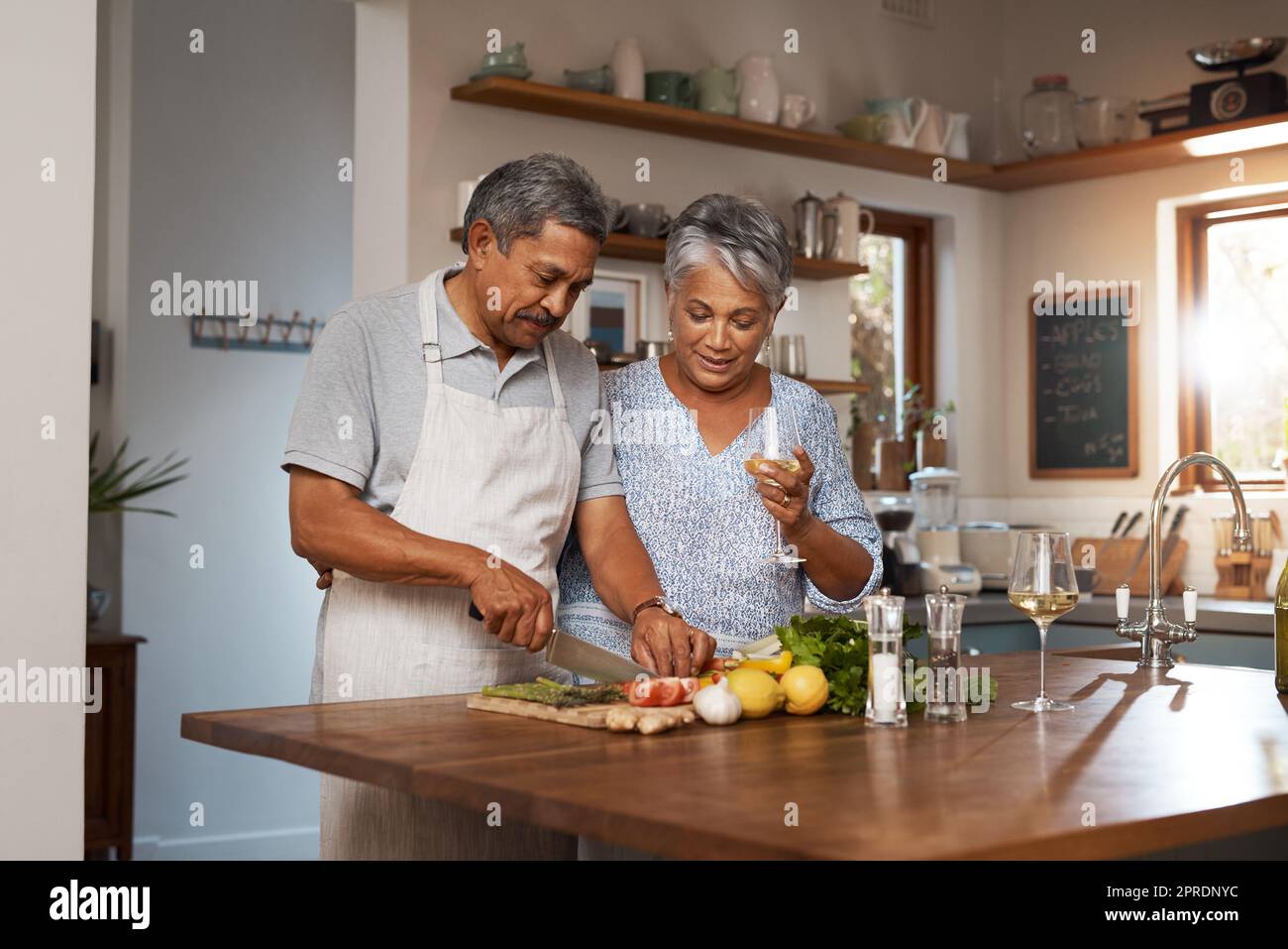 Qu'est-ce que vous faites, le miel. Un couple heureux et mature qui boit du vin tout en cuisinant un repas ensemble à la maison. Banque D'Images